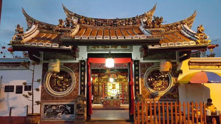 The ornate entrance of Cheng Hoon Teng Temple in Malacca, featuring a beautifully curved roof, intricate carvings, and traditional Chinese architectural details at dusk.
